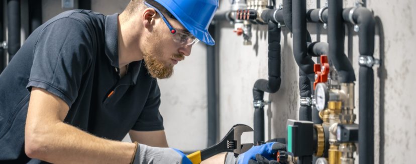 A man installs a heating system in a house and checks the pipes with a wrench. Adjusting heating valves in a residential building. A plumbing and heating technician works.
