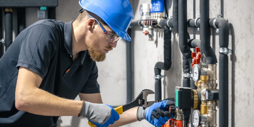 A man installs a heating system in a house and checks the pipes with a wrench. Adjusting heating valves in a residential building. A plumbing and heating technician works.