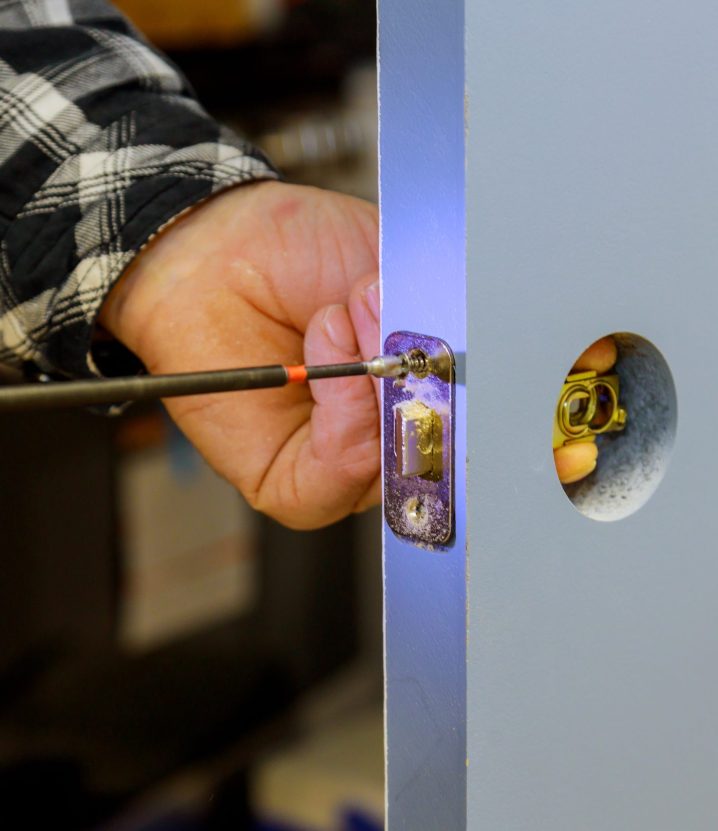 Handyman using a screwdriver drill to installing lock in door in a house