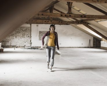 Young woman on construction site carrying ladder and paint bucket